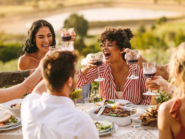 Gruppe fröhlicher Freunde, die bei einer Dinnerparty Wein trinken. Multiethnische Menschen, die draußen zusammenkommen.