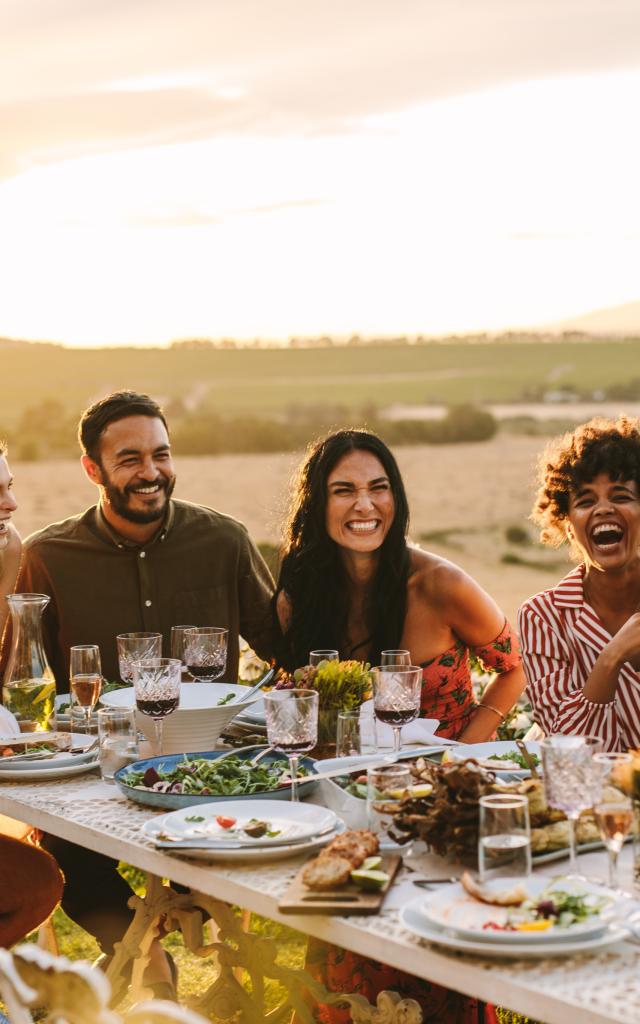 Group of men and women posing for a photograph during an outdoor dinner party. Woman hands taking picture of her friends at dinner party.