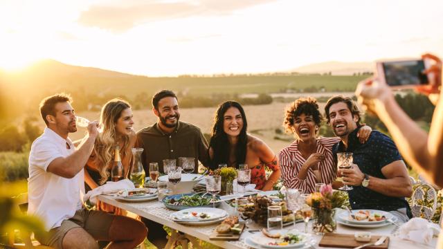 Group of men and women posing for a photograph during an outdoor dinner party. Woman hands taking picture of her friends at dinner party.