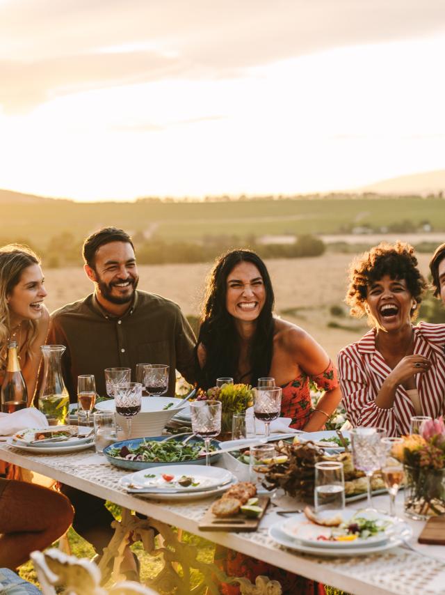 Group of men and women posing for a photograph during an outdoor dinner party. Woman hands taking picture of her friends at dinner party.